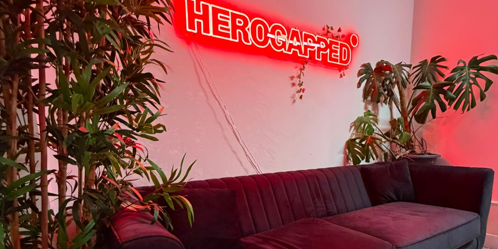 Burgundy sofa beneath the red HeroGapped neon sign in the waiting area