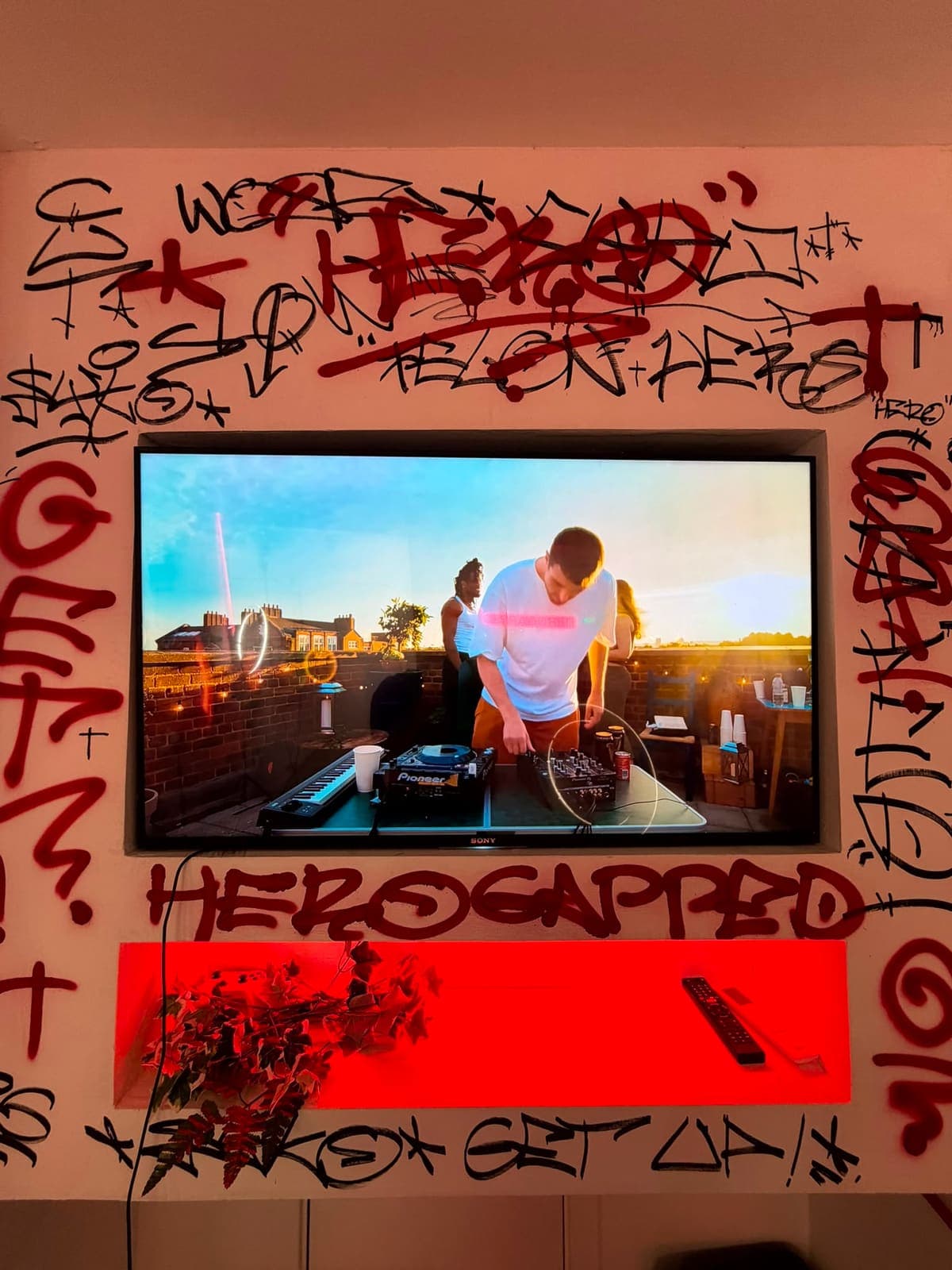 Graffiti-tagged TV wall with the HeroGapped tag under red backlighting