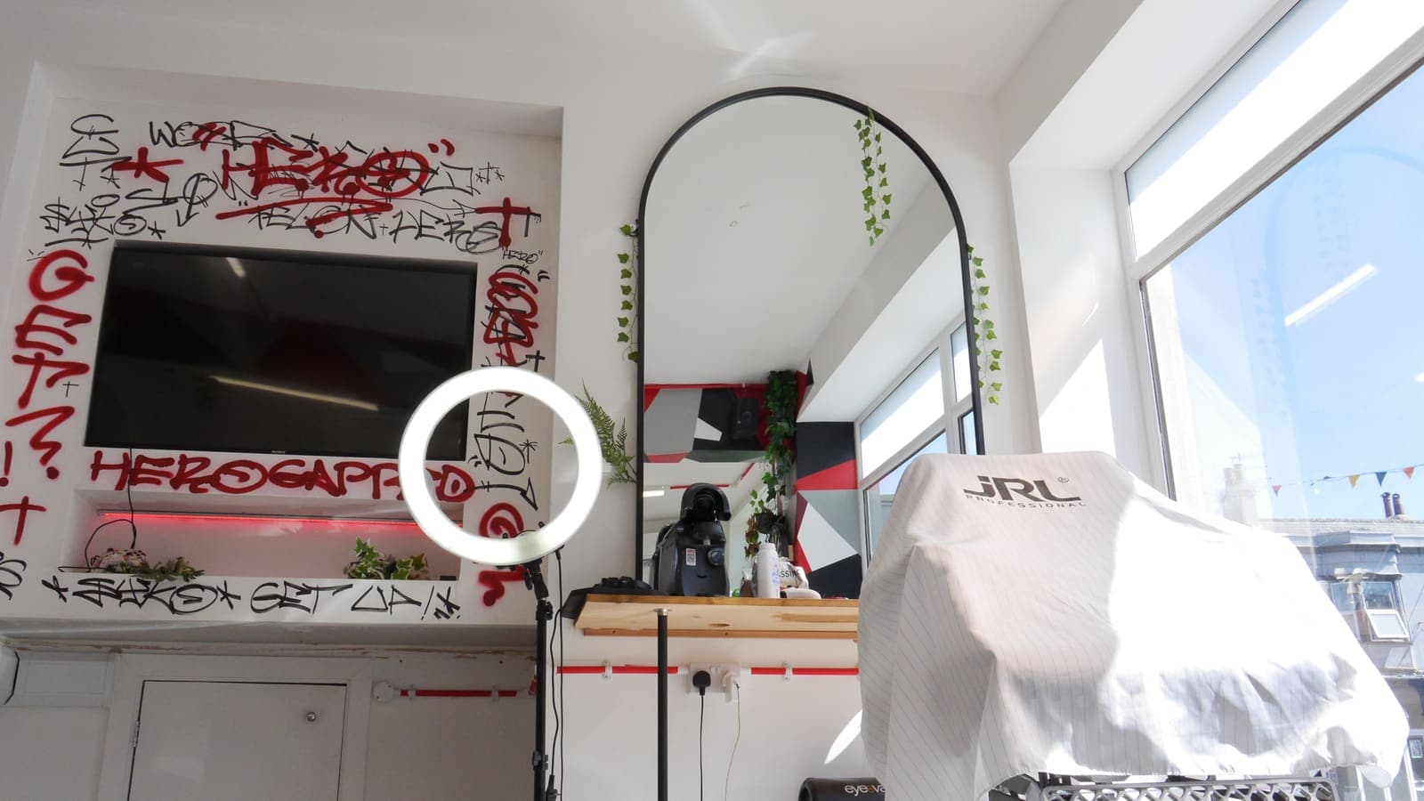 Daylight shopfloor with the graffiti TV wall, arched mirror and caped chair